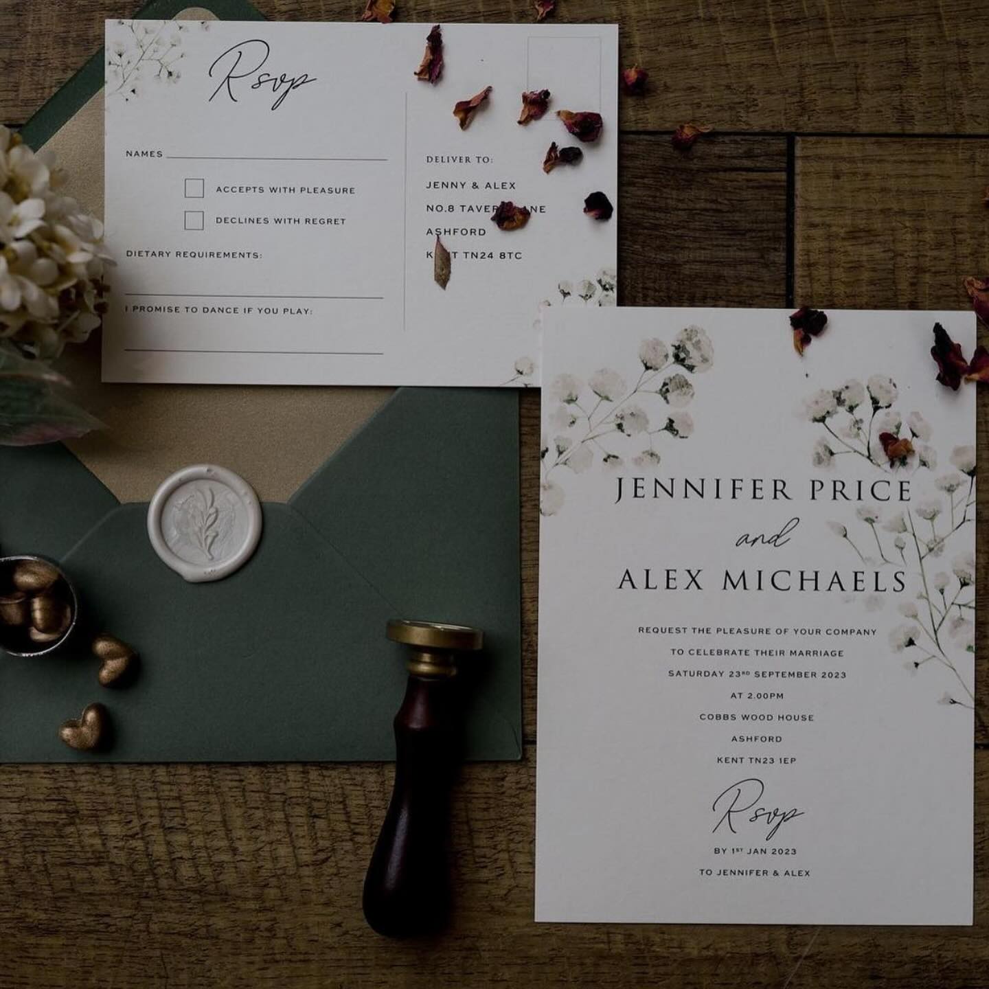 Flat lay of a minimalist single card wedding invitation with baby's breath floral design, matching RSVP postcard, green envelope with wax seal, and gold wax stamp.