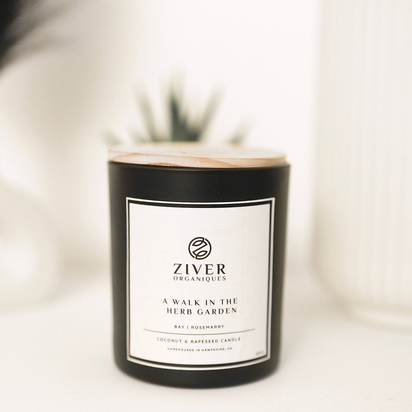Herbal garden scented candle in glass jar on wooden table with plant