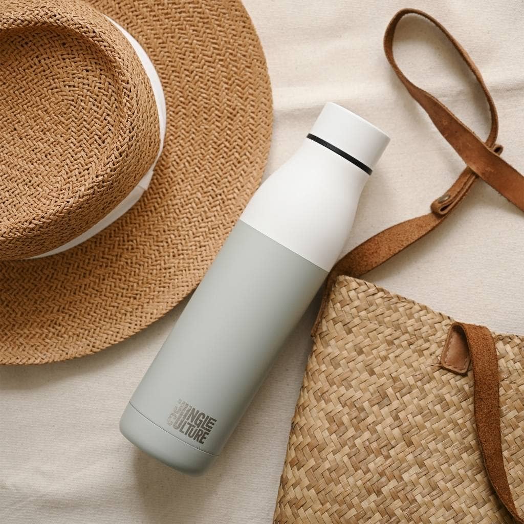 Insulated stainless steel water bottle laid flat on a beg with a bag and straw hat