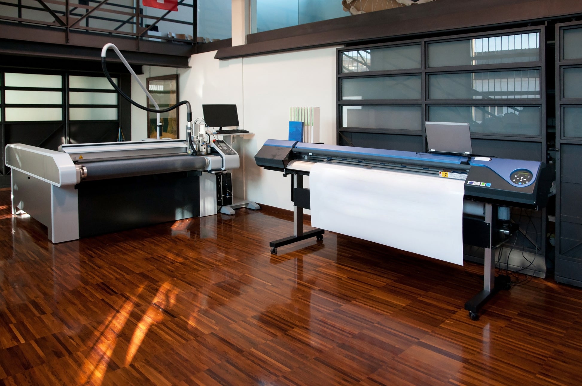 Professional wide-format printers in a modern print studio with wooden flooring, used for producing large signage and mounted wedding table plans.