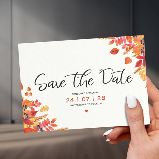 orange and red save the date card held in a hand with painted white names, held up against a stylish sleek room background
