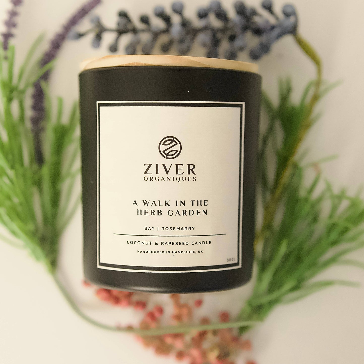 Herbal garden scented candle in glass jar on wooden table with herbs