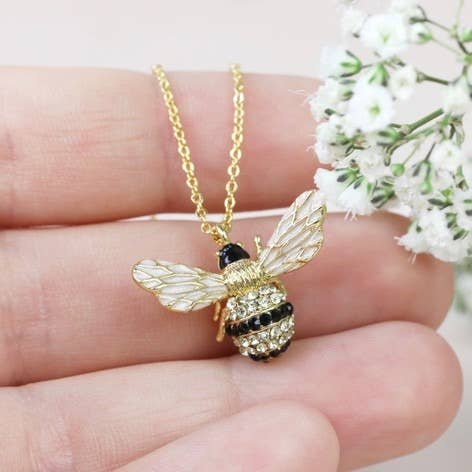 Gold bee pendant necklace with crystal embellishments on neutral background