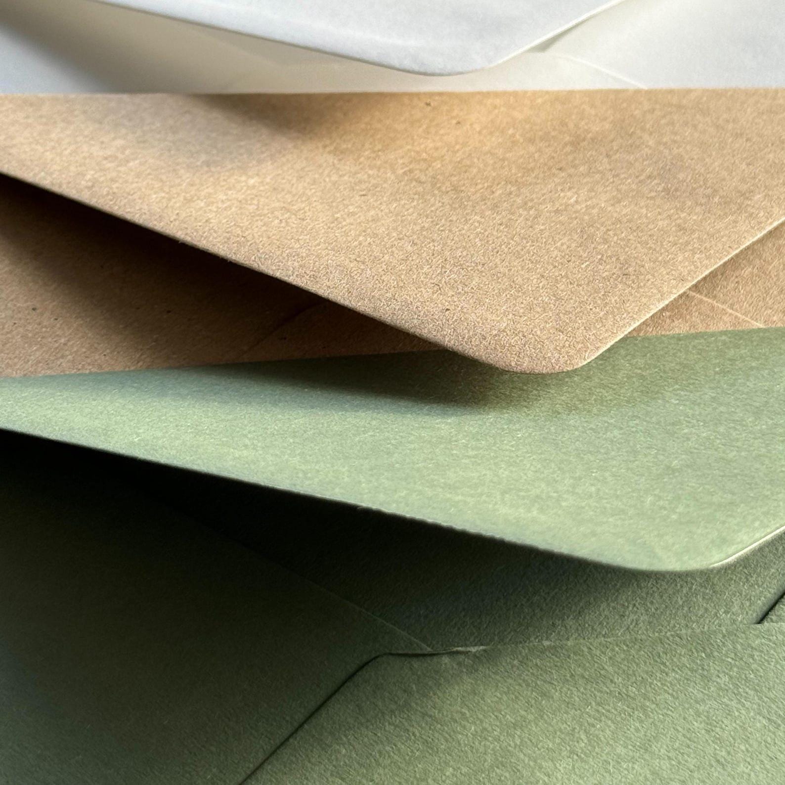 Close-up of textured envelopes in white, kraft, and sage green tones, stacked with overlapping pointed flaps.