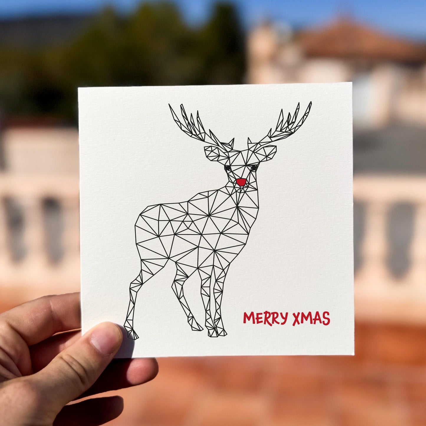 Modern Christmas card featuring a geometric reindeer with red nose and the text ‘Merry Xmas’.