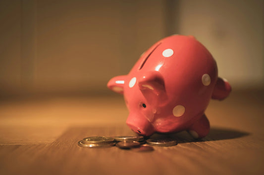 Pink ceramic piggy bank with white polka dots sitting on a wooden surface, with coins placed in front, symbolising saving money or budgeting.