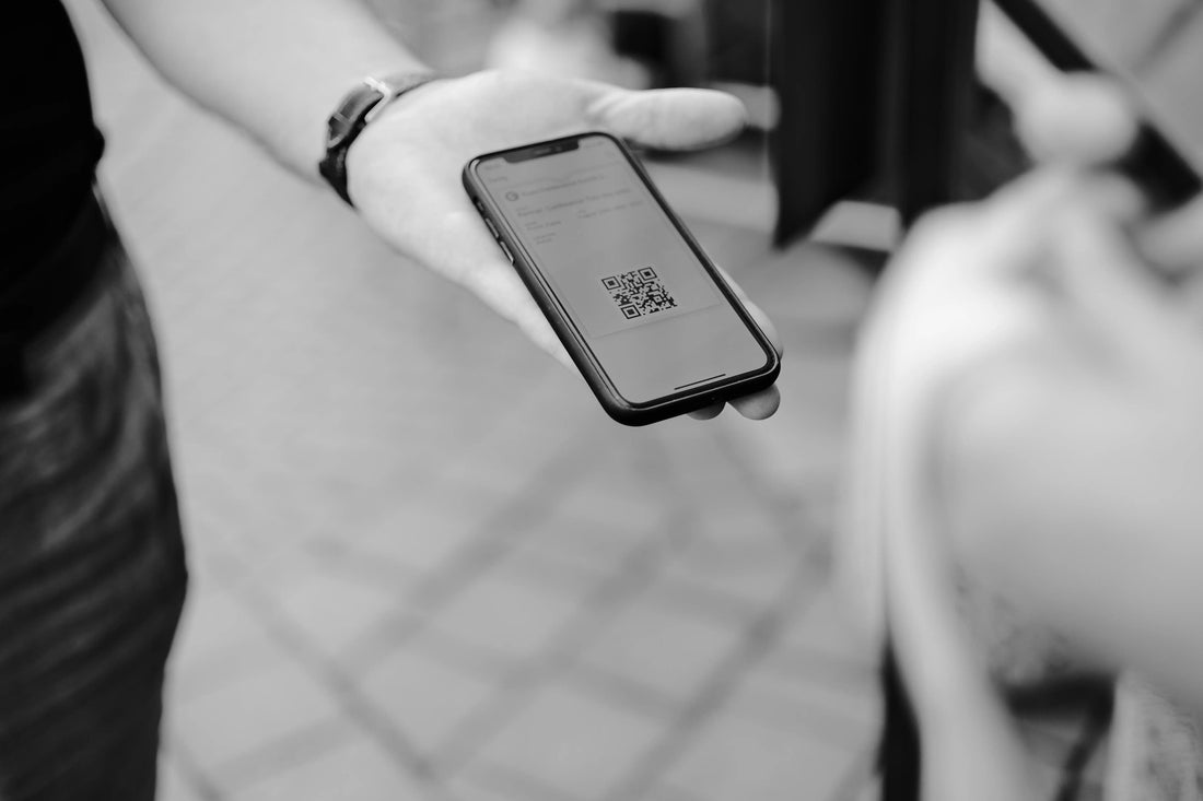 Black and white photo of a person holding a smartphone displaying a QR code, representing digital RSVPs or mobile wedding information.