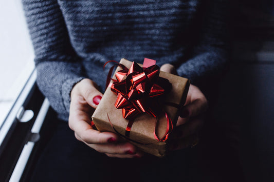 a close up of women's hands holding a little present with a red bow