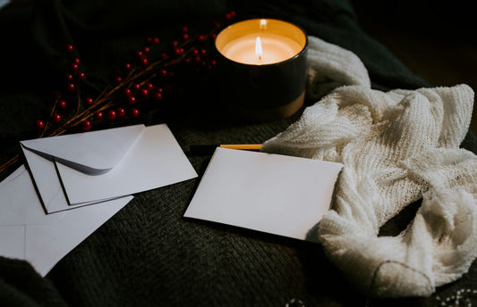 Flat lay of blank white envelopes and cards with a lit candle, white knit fabric and winter berries, styled for cosy wedding stationery planning.