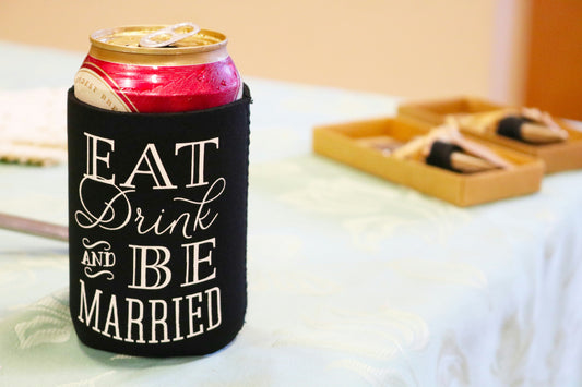 A wedding day table with a can of beer inside a eat drink and be married coozie 