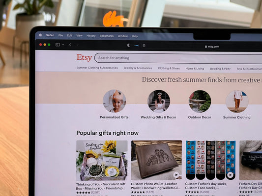 Laptop screen displaying the Etsy homepage with wedding and personalised gift categories, shown on a desk in a bright home workspace.