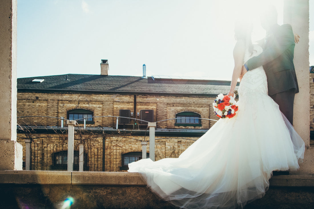 a bride and groom stood in sunlight in front of their wedding venue