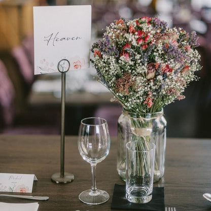 Wedding table name card reading “Heaven” with floral design, displayed on a metal holder next to a mason jar bouquet and formal glassware.