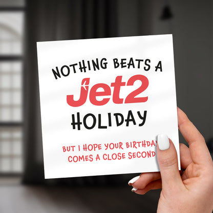 Funny Jet2 holiday themed birthday card printed on textured white card with bold red Jet2 logo and humorous text, held in hand against blurred background