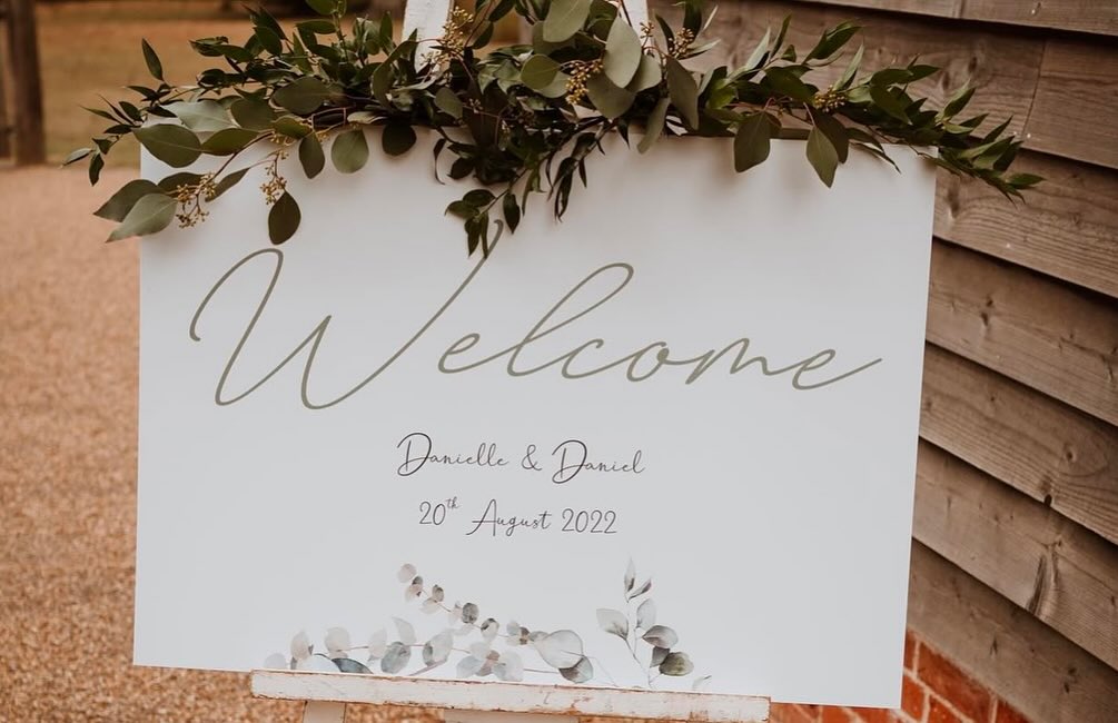 Personalised wedding welcome sign with eucalyptus foliage, featuring sage green script and couple’s names. Elegant rustic welcome sign for outdoor weddings.