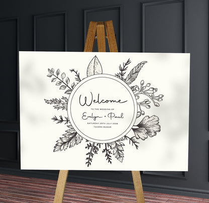 black and white floral sketch wreath A1 welcome sign board on a brown easel in a wedding venue room with stylish decor