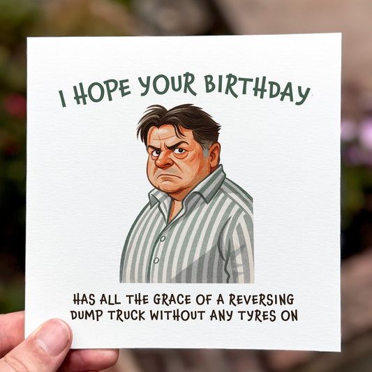 Funny Come Dine With Me birthday card featuring illustration of angry man in striped shirt with quote ‘I hope your birthday has all the grace of a reversing dump truck without any tyres on’, held in hand against blurred background