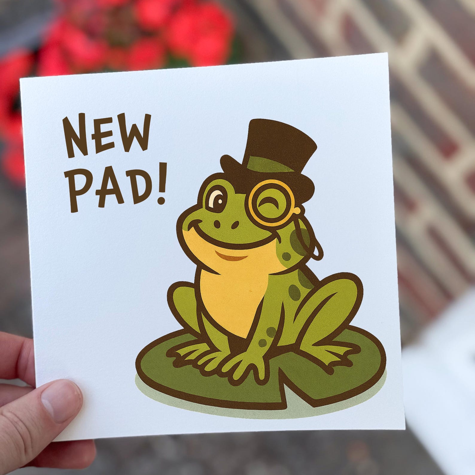New home card featuring a cartoon frog with a top hat and monocle on a lily pad with the text ‘New Pad’.