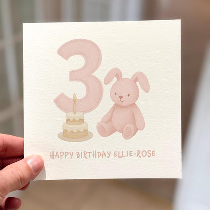 3rd birthday card showing a pink bunny and birthday cake beside number three, text reads ‘Happy Birthday’.