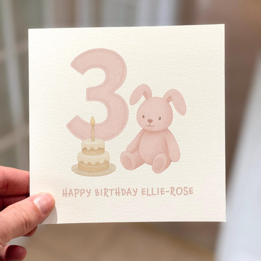 3rd birthday card showing a pink bunny and birthday cake beside number three, text reads ‘Happy Birthday’.