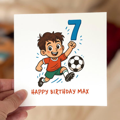 Birthday card featuring a cartoon boy in a red shirt kicking a football with a large blue number seven, printed on textured white card.