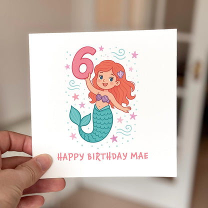 Mermaid-themed birthday card featuring a smiling mermaid holding a pink number six surrounded by shells and stars.