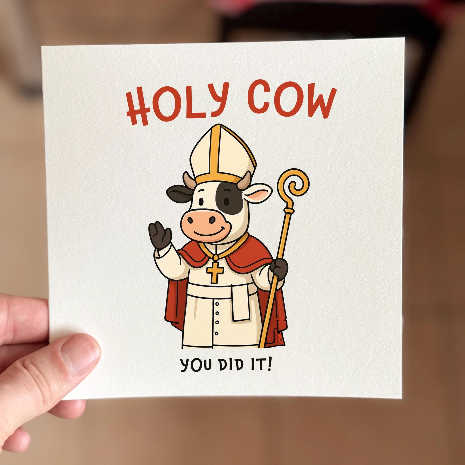 Funny congratulations card featuring a cartoon cow in bishop robes with the text ‘Holy Cow You Did It’.