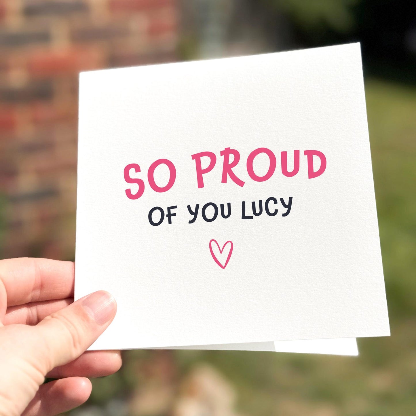 Congratulations card featuring the text ‘So Proud Of You’ with a small heart illustration.
