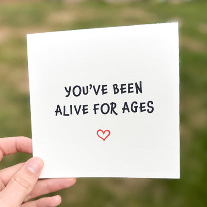 Funny minimalist birthday card with the text ‘You’ve been alive for ages’ and a small red heart underneath.