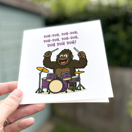 Funny birthday card showing a cartoon gorilla drumming enthusiastically on a purple drum kit with music text above.
