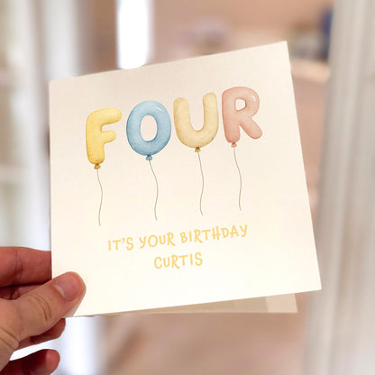 Children’s birthday card with the word ‘FOUR’ written in pastel balloons and space for personalised name.