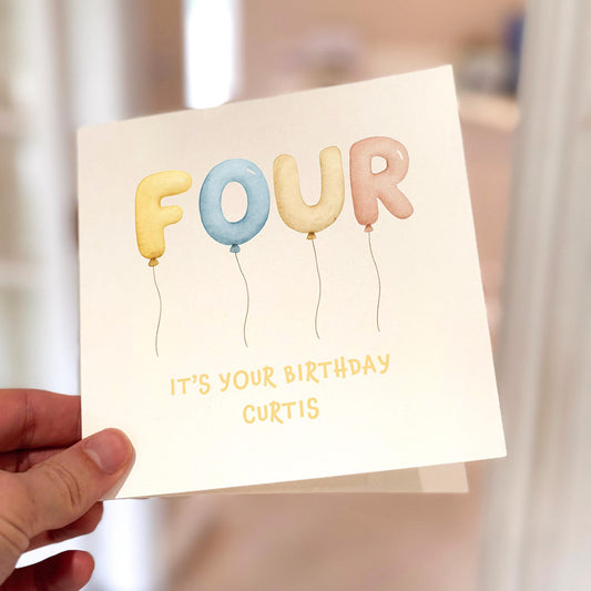 Children’s birthday card with the word ‘FOUR’ written in pastel balloons and space for personalised name.