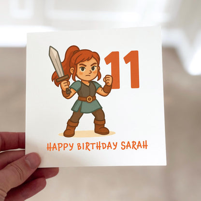 Birthday card featuring a cartoon warrior with a sword standing next to the number eleven, printed on textured white card.