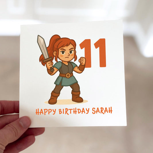 Birthday card featuring a cartoon warrior with a sword standing next to the number eleven, printed on textured white card.