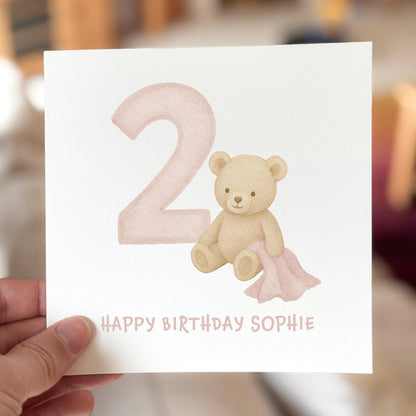 Birthday card featuring a teddy bear with a pink number two, printed on white textured card.