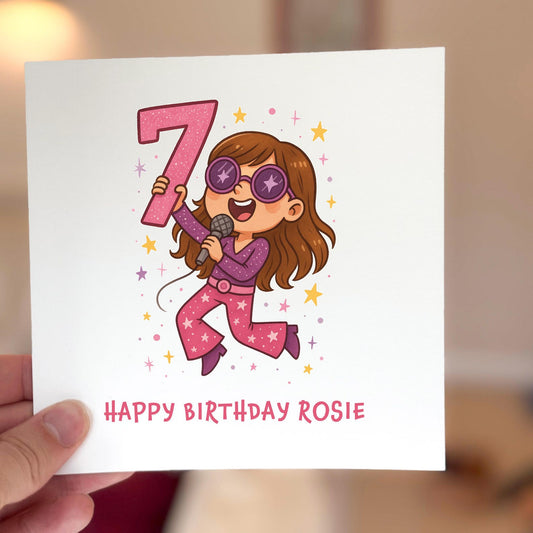Birthday card featuring a cartoon popstar holding a microphone and a number seven, surrounded by stars.