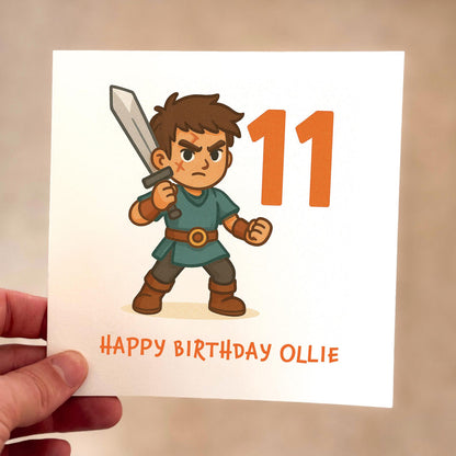 Birthday card featuring a cartoon warrior holding a sword with a large orange number eleven, printed on textured card.