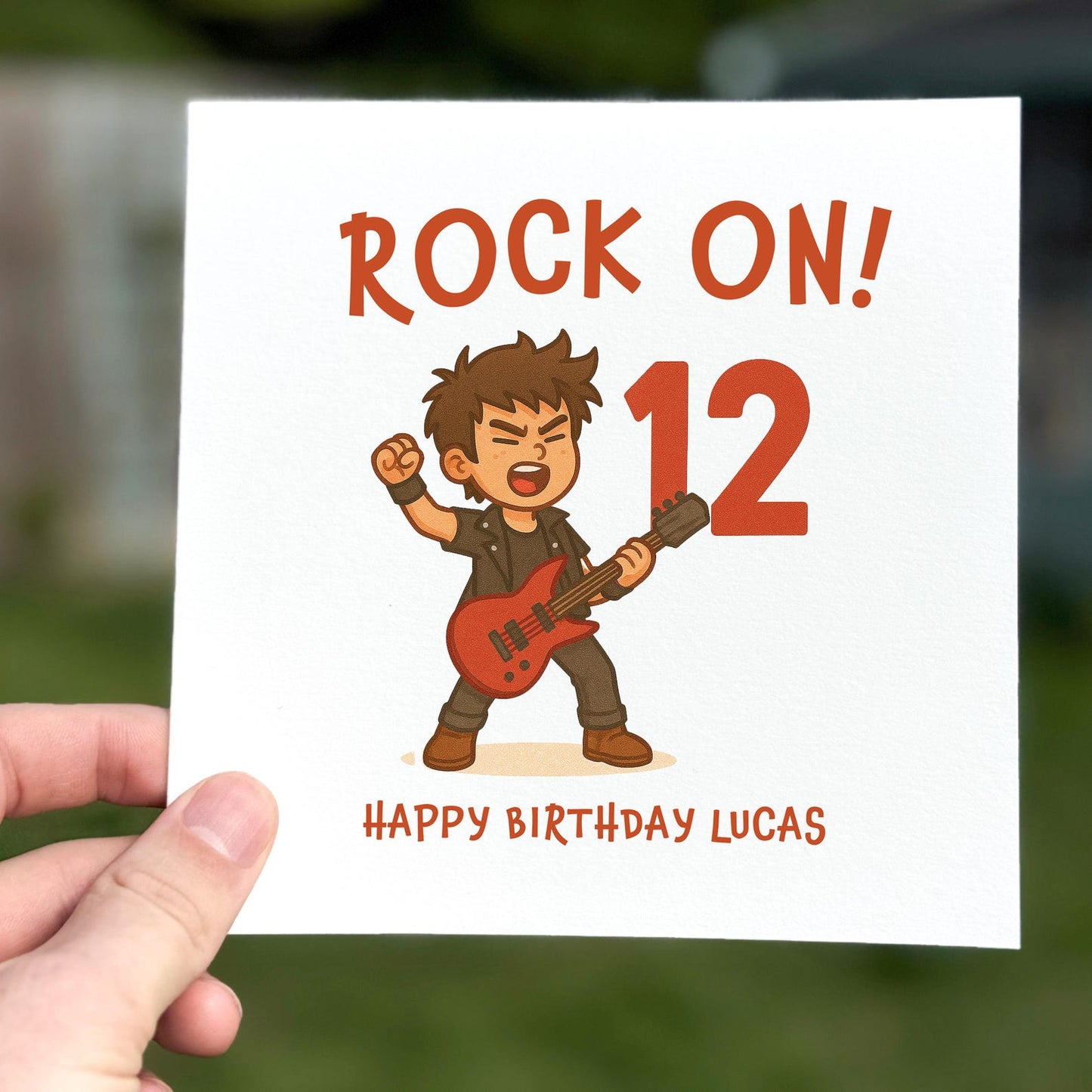 Birthday card featuring a cartoon rock guitarist holding a red guitar with the words ‘Rock On!’ and a large red number.