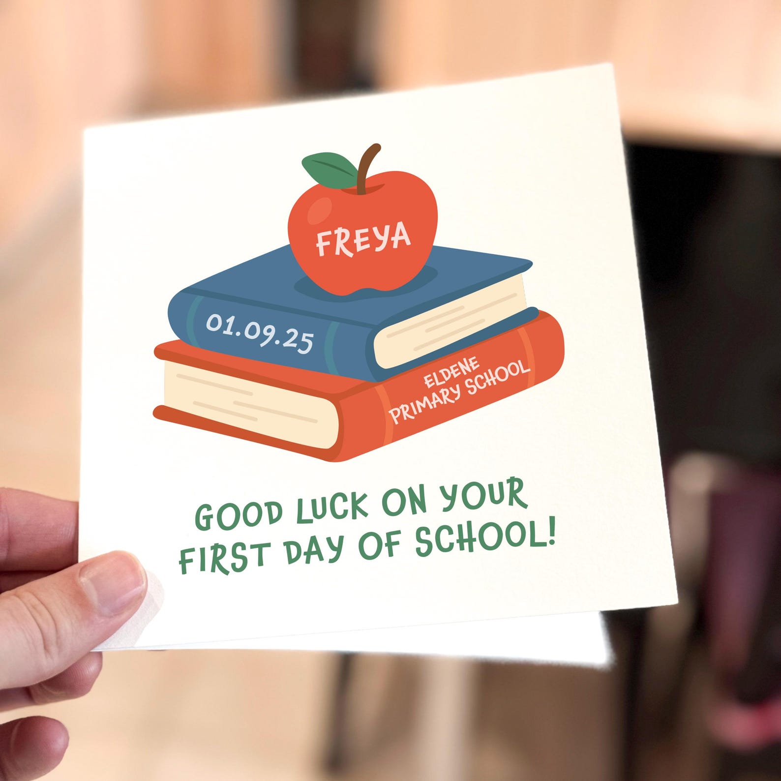 Good luck school card featuring a red apple on stacked books illustration with green text.