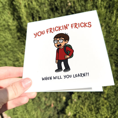 Funny greeting card showing a cartoon boy shouting 'You Frickin’ Fricks – When will you learn?!' held outdoors in natural light.