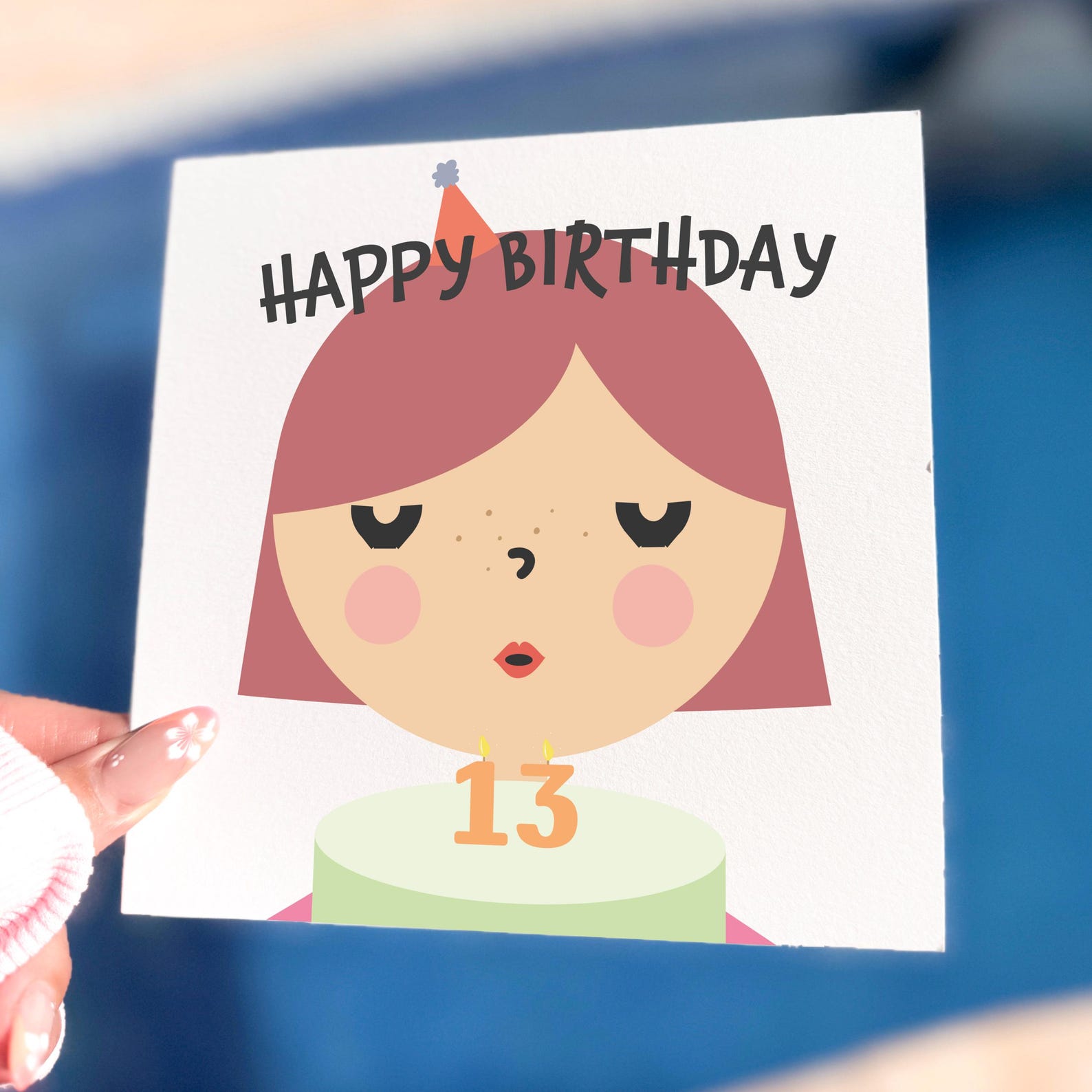 Illustrated 13th birthday card featuring a girl in a party hat blowing out candles on a cake with the number 13.