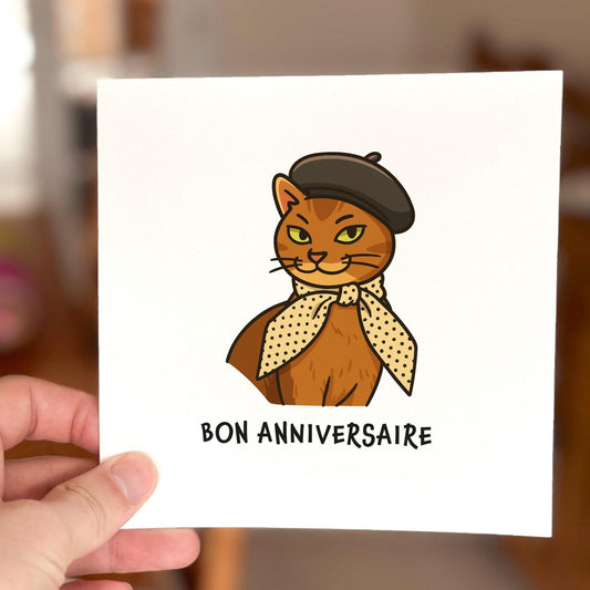 French-inspired birthday card featuring a cartoon cat wearing a beret and scarf with the words 'Bon Anniversaire'.