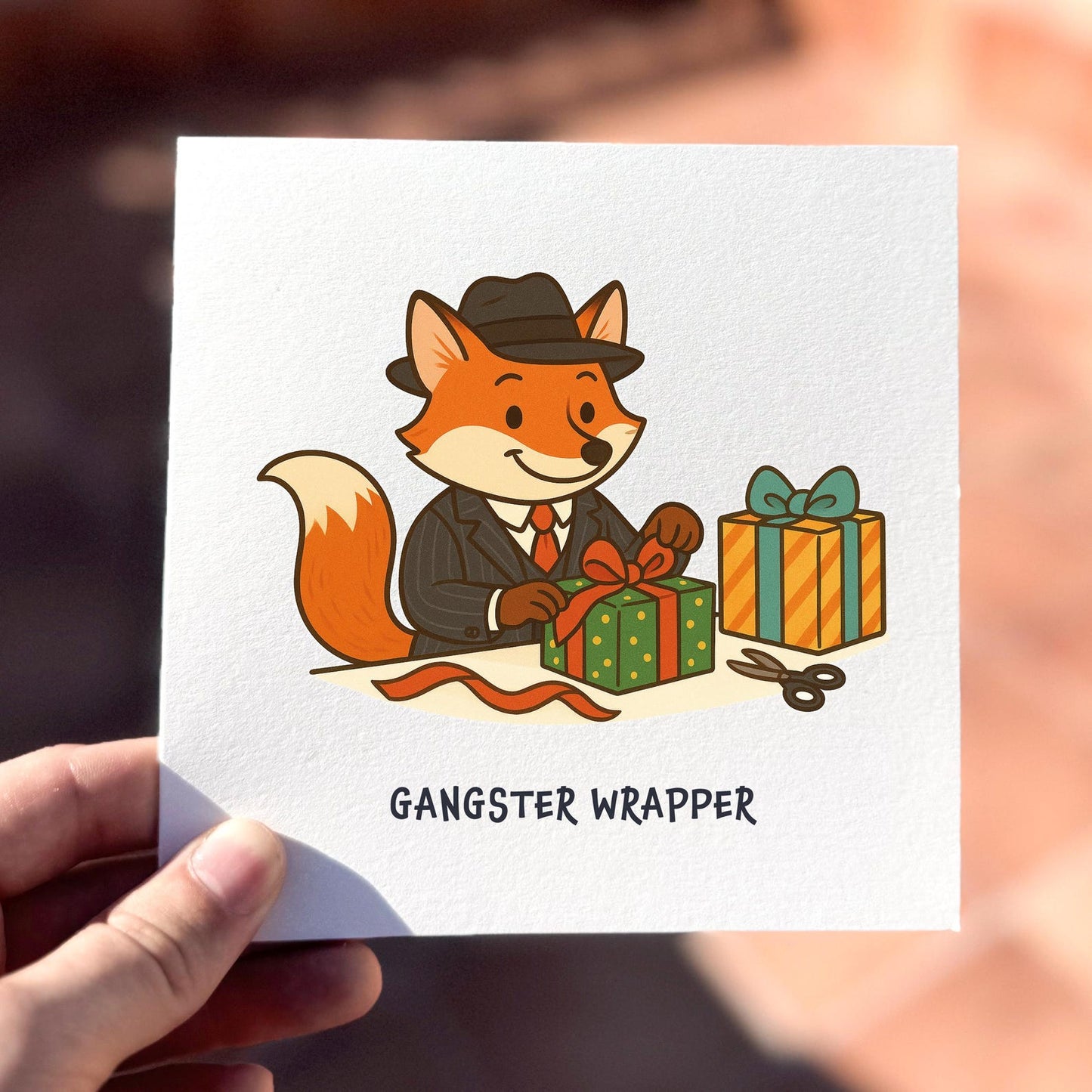 Funny Christmas card featuring a fox in a suit wrapping presents with the text ‘Gangster Wrapper’.