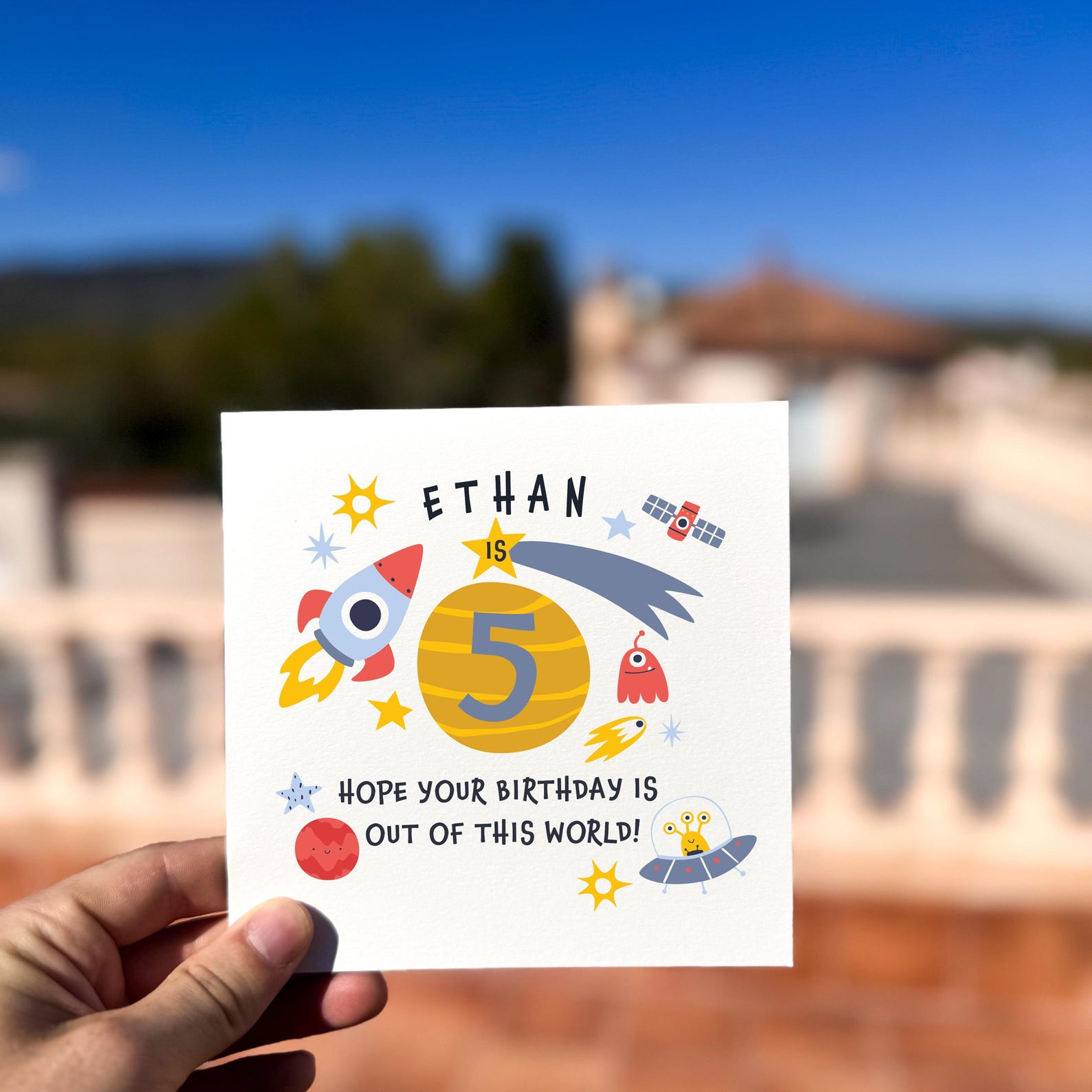 Birthday card featuring colourful rockets, planets and stars with the text ‘Out of This World’, printed on textured card.