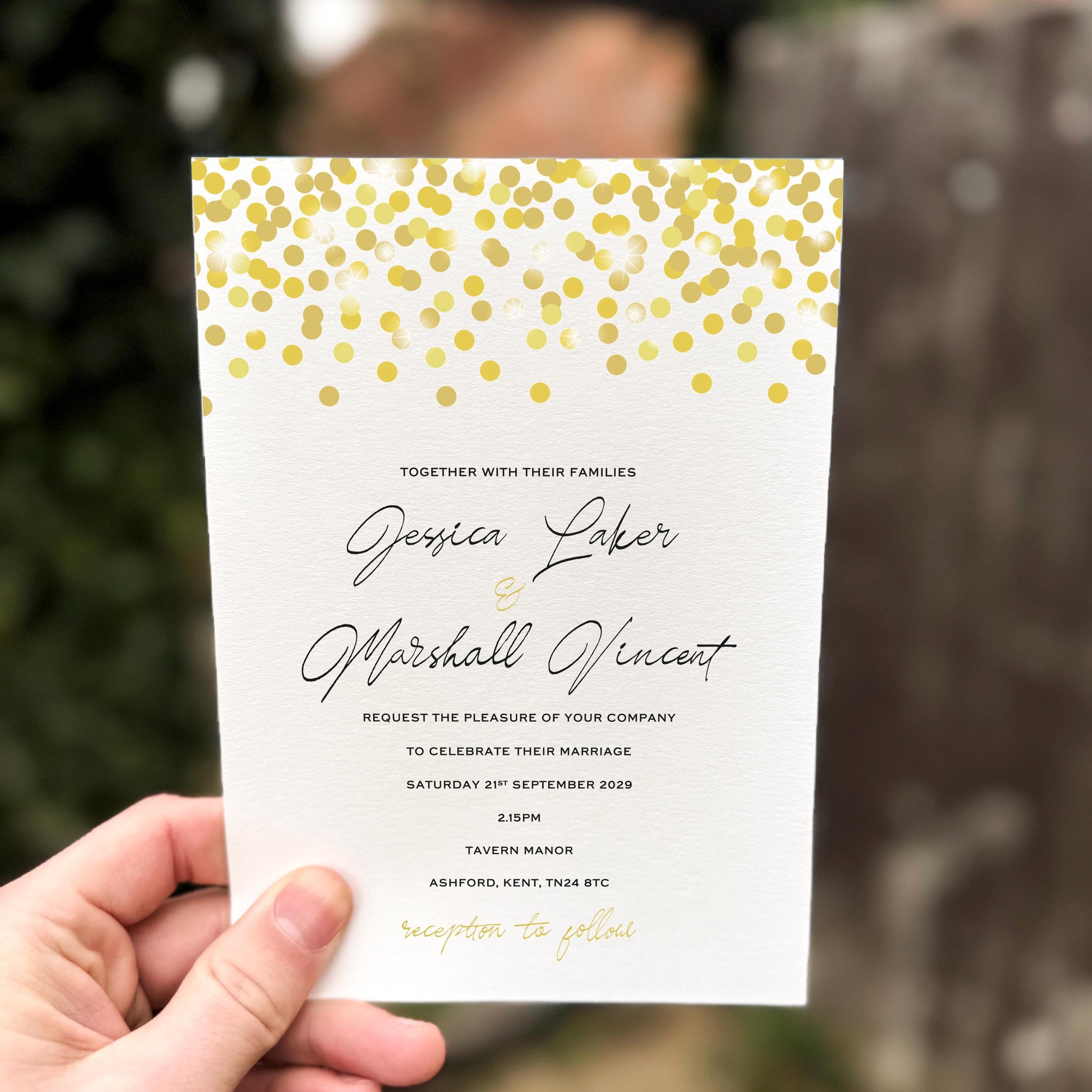 Hand holding a wedding invitation featuring scattered gold confetti dots across the top with elegant script text.