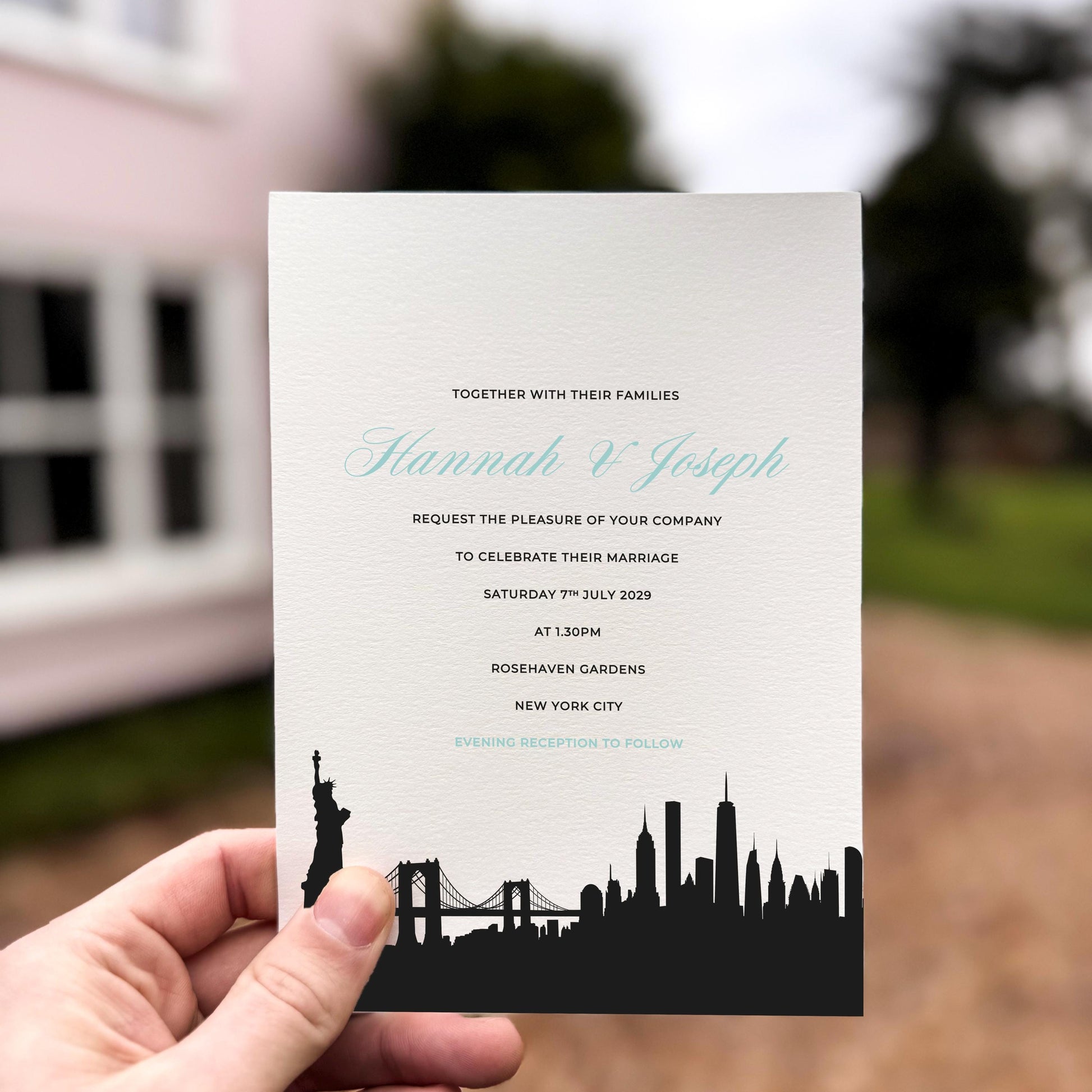 Hand holding a wedding invitation featuring a black silhouette of the New York City skyline, including the Statue of Liberty and Brooklyn Bridge.