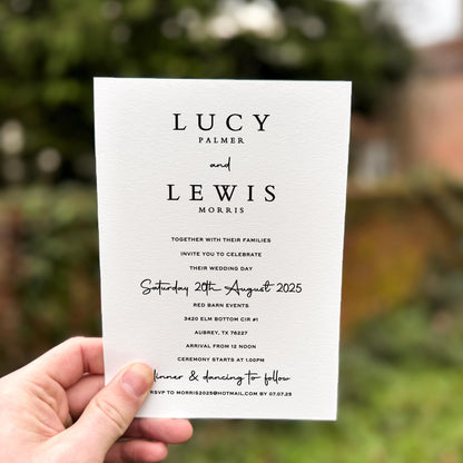 Hand holding a wedding invitation featuring bold serif names, clean black text and handwritten script accents on premium textured card.