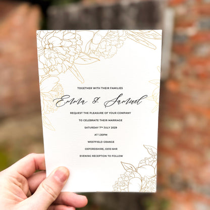 Hand holding a wedding invitation featuring delicate gold line-art florals with a minimalist layout and modern script names.