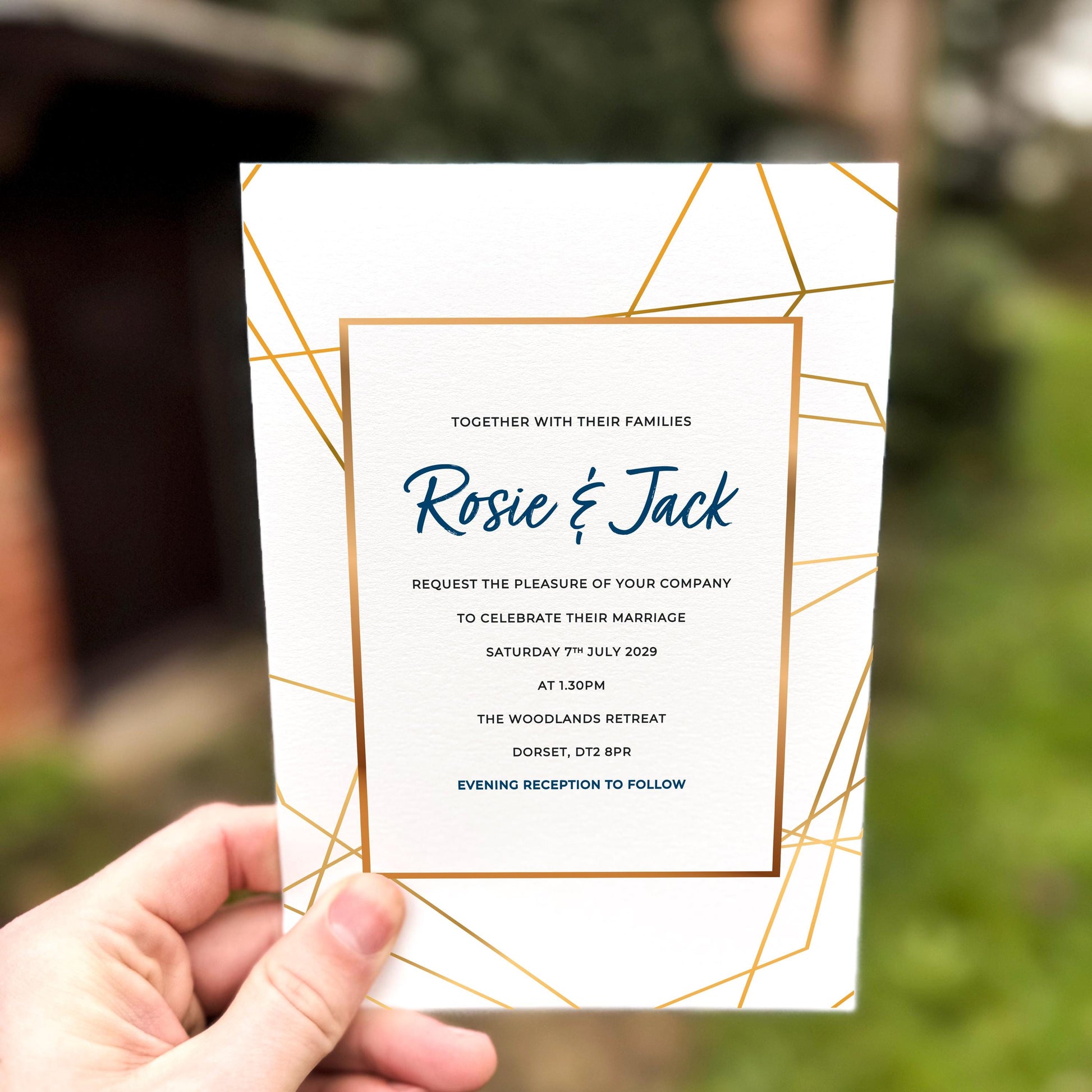 Hand holding a wedding invitation featuring modern gold geometric linework framing elegant navy text.