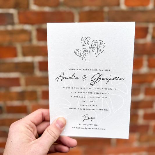 Hand holding a wedding invitation featuring minimalist monstera leaf line art with elegant black script text.